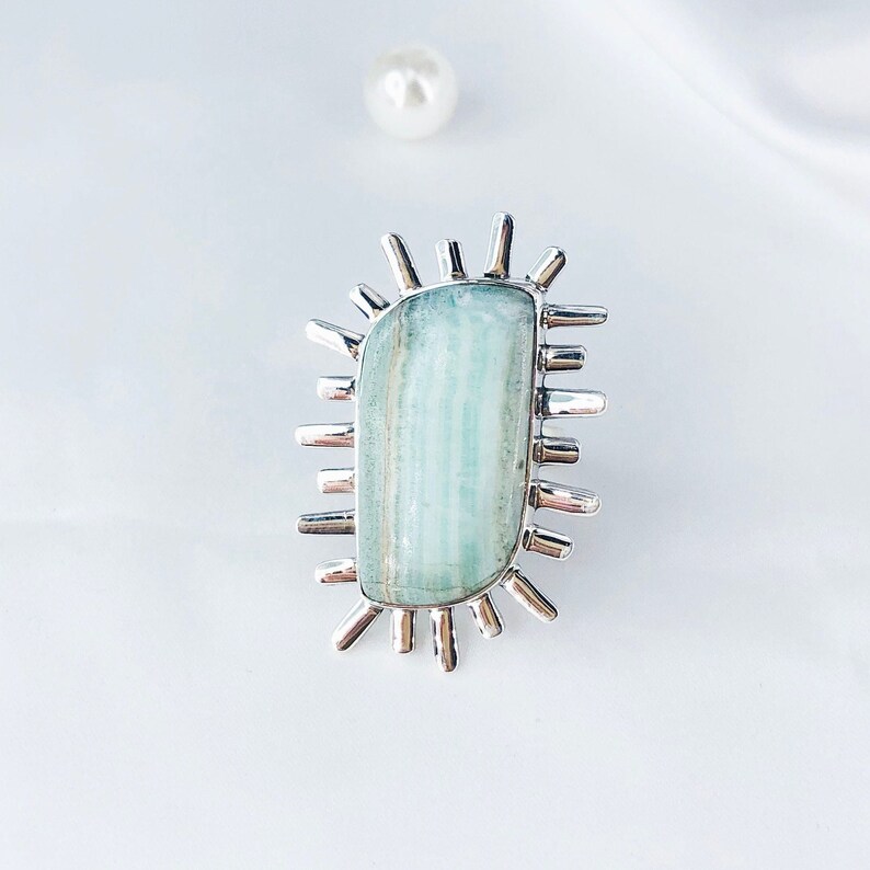 K&ouml;nnte beinhalten: Ein silberner Ring mit einem hellblauen Aquamarin-Stein, der in einem Sternburst-Design gefasst ist.