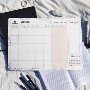 May include: A white dry-erase monthly calendar with a floral design. The calendar has spaces for each day of the week, a to-do list, and a tracker for the month. The calendar is magnetic and can be used on a refrigerator or other metal surface.