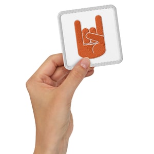 Könnte beinhalten: Ein weißer quadratischer Patch mit grauem Rand, der eine orangefarbene gestickte Hand zeigt, die das Rock'n'Roll-Handzeichen macht.