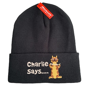 May include: Black beanie hat with a turned-up brim. The hat has the embroidered text "Charlie Says...." and a cartoon cat holding a string. A red tag that says "Result Headwear" is attached.