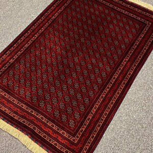 May include: A rectangular red rug with a repeating floral pattern and a detailed border. The rug has a cream-colored fringe on one end. The pattern includes dark red, brown, and gold accents.
