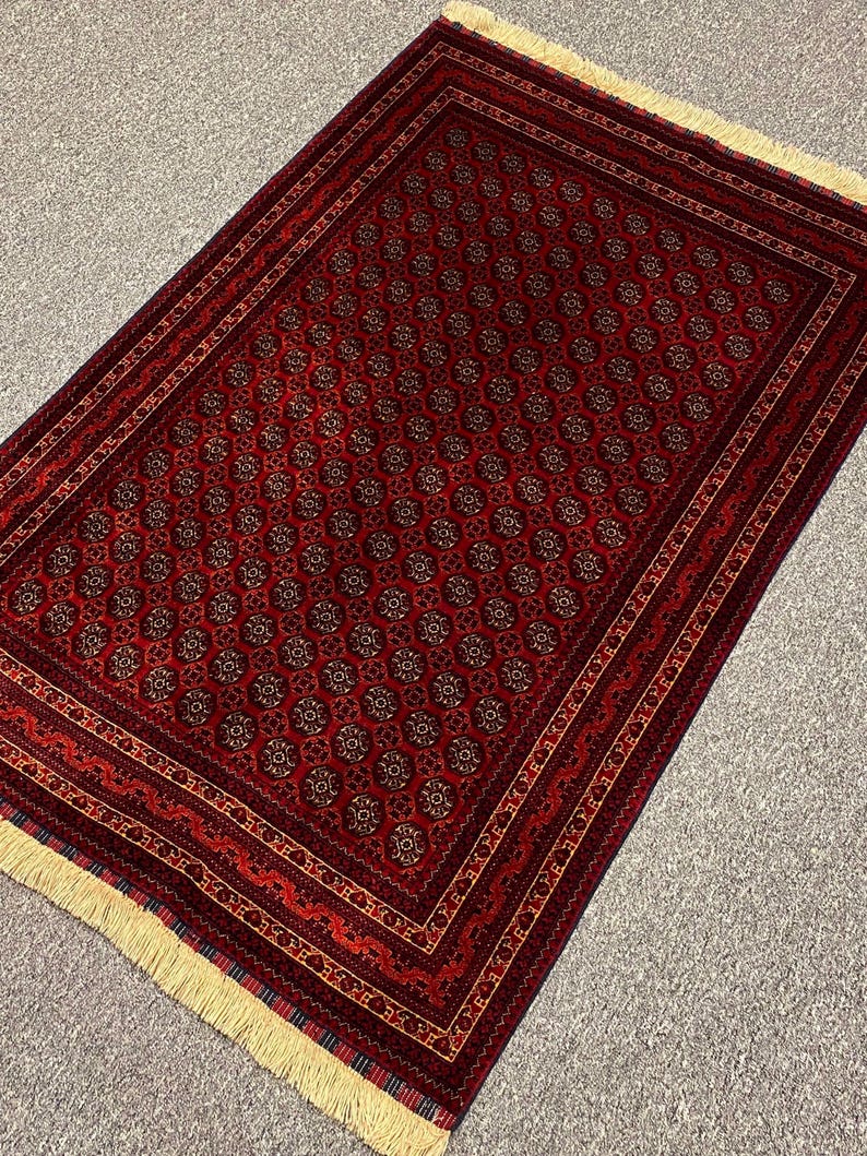 May include: A rectangular red rug with a repeating floral pattern and a detailed border. The rug has a cream-colored fringe on one end. The pattern includes dark red, brown, and gold accents.