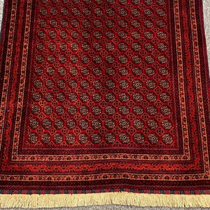 May include: A rectangular, red rug with a repeating circular pattern in shades of brown and gold. The rug has a detailed border with geometric designs and a cream-colored fringe along the bottom edge. The rug is likely made of wool.