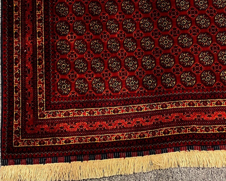 May include: A detailed shot of a red oriental rug with a repeating circular pattern in shades of brown and gold. The rug has a decorative border and a fringe along the bottom edge. The rug's design is intricate and traditional.
