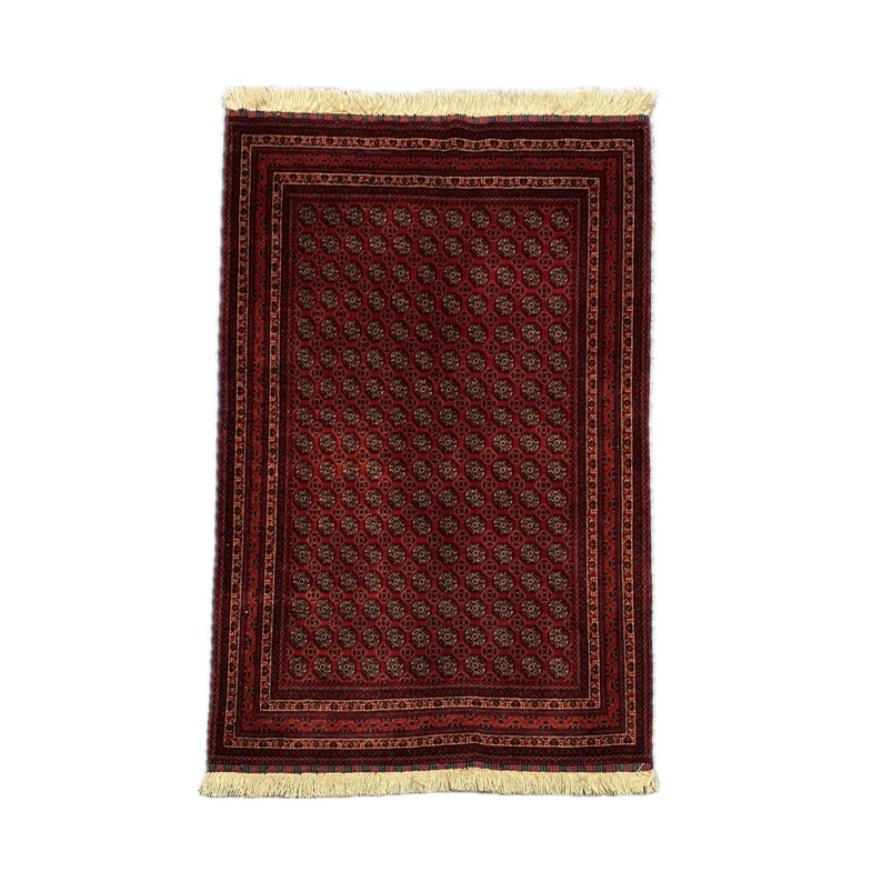 May include: A rectangular, red rug with a repeating pattern of small, circular motifs. The rug has a dark red border and cream-colored fringe along the short edges. The pattern is in shades of brown and gold.
