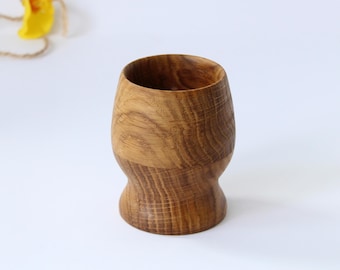 Puede incluir: Un cáliz de madera con una base redondeada y una parte superior ancha y abierta. El cáliz está hecho de madera marrón claro con un patrón de veta natural.