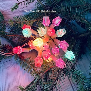 Puede incluir: Una cadena de luces navideñas vintage con bombillas de colores en tonos rosa, verde y amarillo. Las luces están dispuestas en forma de estrella y están rodeadas de ramas de pino.