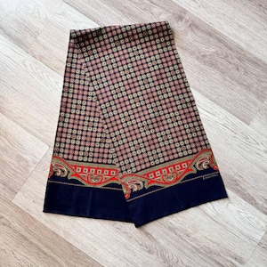 May include: A patterned scarf with a repeating design of red and tan circles on a black background. The scarf has a navy blue border with a red and gold decorative pattern. The scarf is made of a soft material.