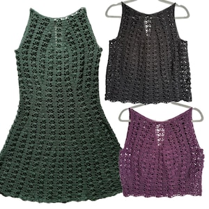 Könnte beinhalten: Drei handgefertigte Häkeltops und ein Kleid in Grün-, Anthrazit- und Lilatönen. Das offene Webmuster ist sichtbar, und die Kleidungsstücke werden auf Kleiderbügeln präsentiert. Das Kleid hat einen Neckholder-Ausschnitt und einen ausgestellten Rock.