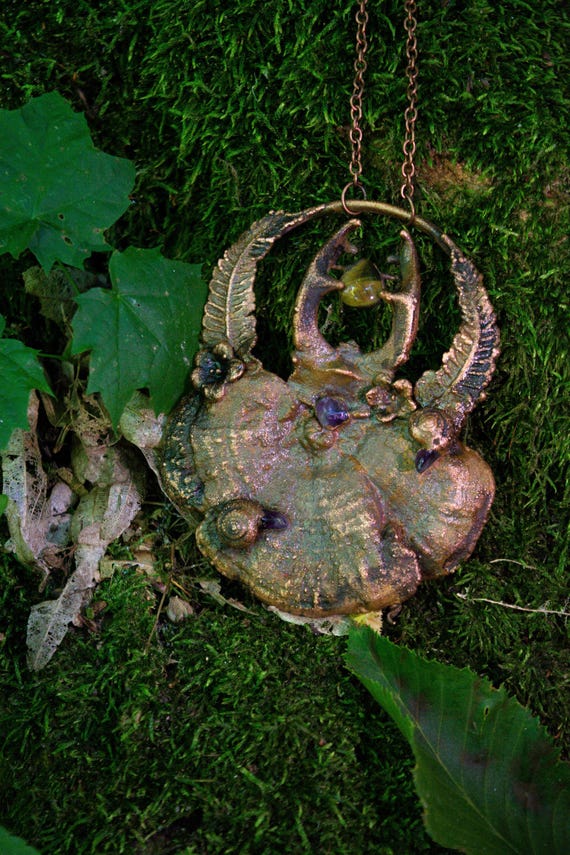 A real beetle encased in electroformed copper alongside a mushroom — wearable woodland witchcraft that no factory is replicating.