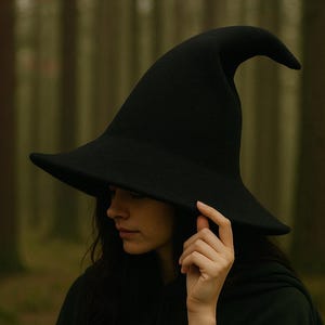 以下が含まれることがあります： つばの広い黒い魔女の帽子と尖った先端。帽子は濃い緑色のマントと一緒に着用されています。背景はぼやけた森のシーンです。帽子はコスチュームアクセサリーです。