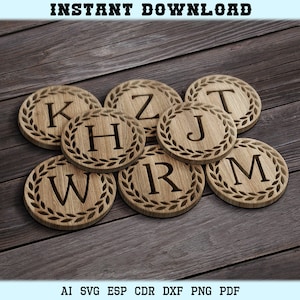 Puede incluir: Posavasos de madera con un diseño de corona de laurel y las letras K, Z, H, J, W, R, M. Los posavasos están apilados sobre una superficie de madera.