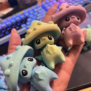 May include: A collection of colorful, whimsical mushroom-shaped figurines. The figurines are in shades of blue, green, and pink, with textured surfaces and large, black eyes. The figures have a unique, cartoonish design.