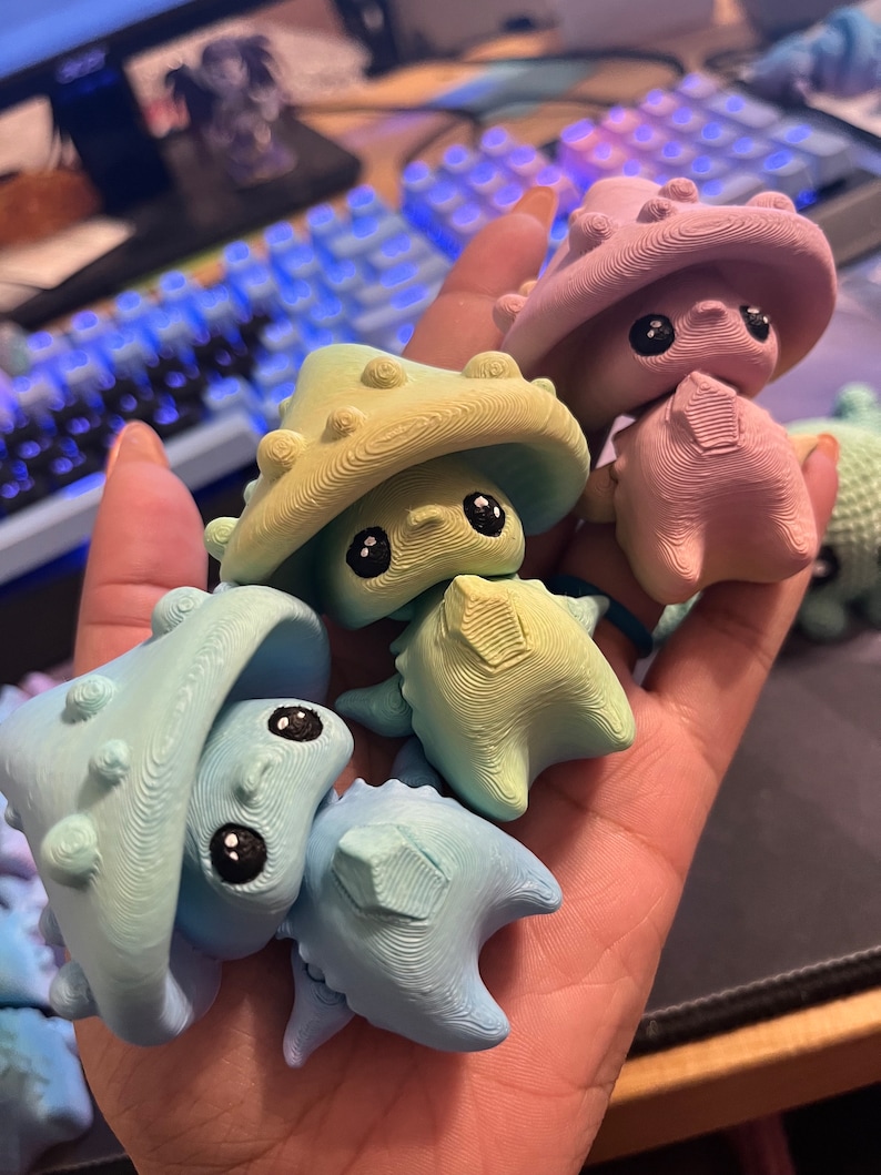 May include: A collection of colorful, whimsical mushroom-shaped figurines. The figurines are in shades of blue, green, and pink, with textured surfaces and large, black eyes. The figures have a unique, cartoonish design.