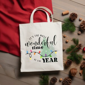 May include: White canvas tote bag with a Christmas-themed design. The bag features the text "It's the most wonderful time of the year" with a stylized Christmas tree and string of lights.