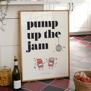 Puede incluir: Un póster enmarcado con las palabras "pump up the jam" en letras negras. El póster presenta botes de mermelada bailando y una ilustración de bola de discoteca. Una cesta de manzanas, una botella de vino y un tarro de pasta están en primer plano.