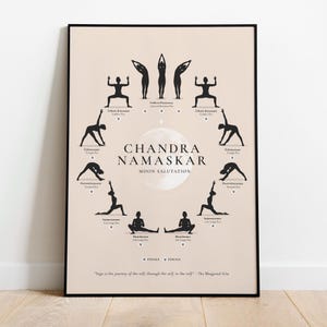 May include: A framed poster featuring a beige background with black silhouettes demonstrating yoga poses. The text "Chandra Namaskar Moon Salutation" is centered, with the quote "Yoga is the journey of the self, through the self, to the self." below.