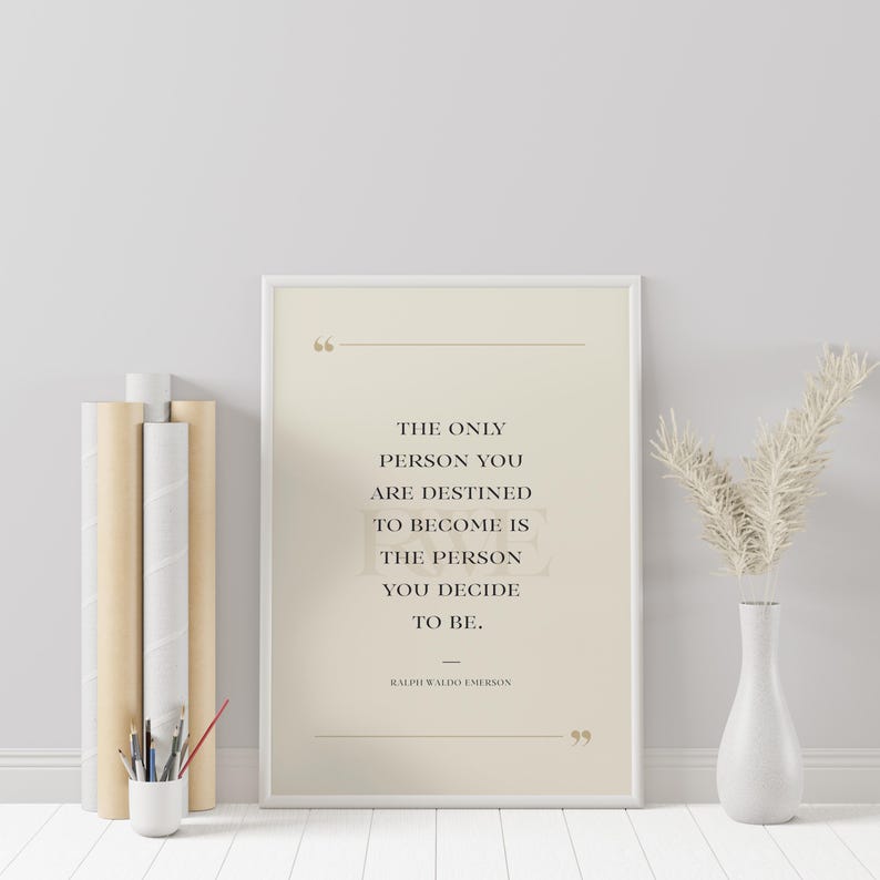 K&ouml;nnte beinhalten: Ein gerahmter Druck mit dem Zitat "THE ONLY PERSON YOU ARE DESTINED TO BECOME IS THE PERSON YOU DECIDE TO BE." von Ralph Waldo Emerson. Der Druck befindet sich in einem hellbeigen Rahmen, mit einer wei&szlig;en Vase und dekorativen Stielen.