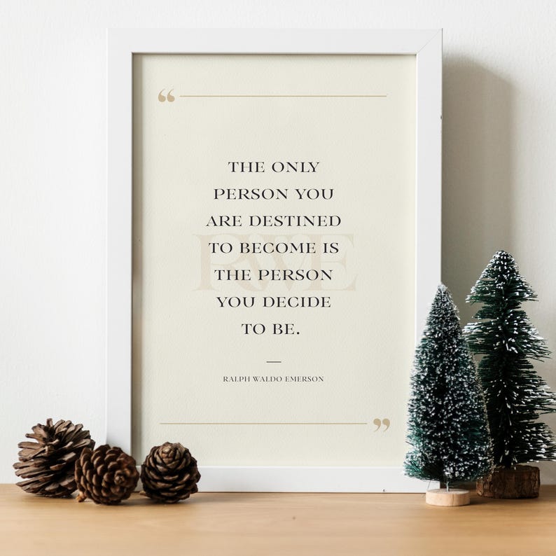 K&ouml;nnte beinhalten: Ein wei&szlig; gerahmter Druck mit dem Zitat "THE ONLY PERSON YOU ARE DESTINED TO BECOME IS THE PERSON YOU DECIDE TO BE." von Ralph Waldo Emerson. Vor dem Rahmen befinden sich Tannenzapfen und kleine Weihnachtsb&auml;ume.
