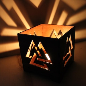 Op de afbeelding: Een zwarte houten kaarsenhouder met een uitgesneden geometrisch ontwerp. De kaarsenhouder is aangestoken en geeft een warm licht.
