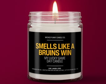 May include: A white candle in a glass jar with a black label that reads "WICKED FUNNY CANDLE CO. SMELLS LIKE A BRUINS WIN MY LUCKY GAME DAY CANDLE LIVE. LAUGH. LOVE. HANDMADE IN THE USA | CRAFTED FROM 100% NATURAL SOY WAX | UP TO 60 HR BURN TIME | 9 OZ"