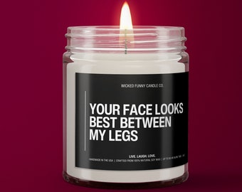 May include: A white candle in a clear glass jar with a black label that reads "WICKED FUNNY CANDLE CO. YOUR FACE LOOKS BEST BETWEEN MY LEGS LIVE. LAUGH. LOVE. HANDMADE IN THE USA | CRAFTED FROM 100% NATURAL SOY WAX | UP TO 60 HOUR BURN TIME | 10 OZ"