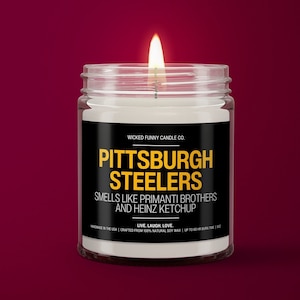 May include: A white candle in a clear glass jar with a black label that reads "WICKED FUNNY CANDLE CO. PITTSBURGH STEELERS SMELLS LIKE PRIMANTI BROTHERS AND HEINZ KETCHUP LIVE. LAUGH. LOVE. HANDMADE IN THE USA | CRAFTED FROM 100% NATURAL SOY WAX | UP TO 60 HR BURN TIME | 8 OZ"