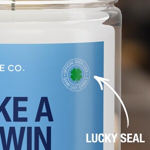 Puede incluir: Un tarro de vela azul y blanco con el texto "Take a Win" y una pegatina de tr&eacute;bol de cuatro hojas verde con el texto "Official Good Luck Game Day Candle".