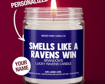 May include: A personalized candle with a blue label that reads "Smells Like A Ravens Win" and "Brandon's Lucky Ravens Candle". The candle is in a clear glass jar with a white wax interior and a lit wick.