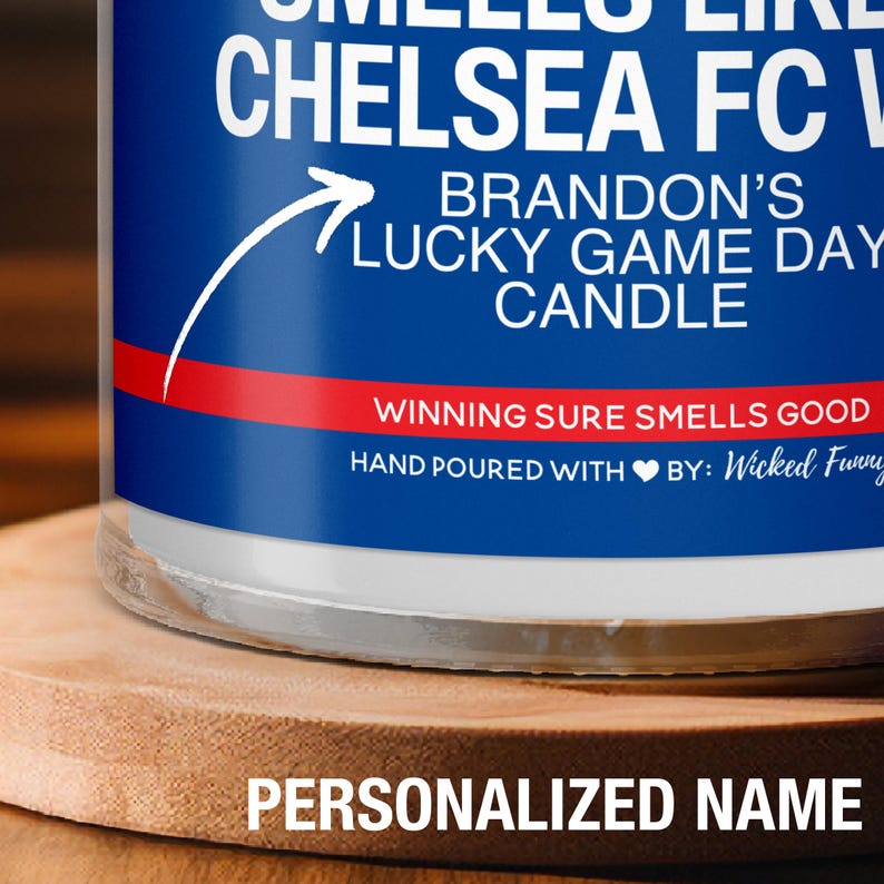 May include: A blue and red candle with the text "CHELSEA FC" and "BRANDON'S LUCKY GAME DAY CANDLE". The text "WINNING SURE SMELLS GOOD" is on a red stripe. The candle is on a wooden surface.
