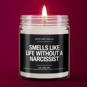 May include: A white candle in a glass jar with a black label that reads "WICKED FUNNY CANDLE CO. SMELLS LIKE LIFE WITHOUT A NARCISSIST LIVE. LAUGH. LOVE. HANDMADE IN THE USA | CRAFTED FROM 100% NATURAL SOY WAX | UP TO 60 HR BURN TIME | 9OZ"
