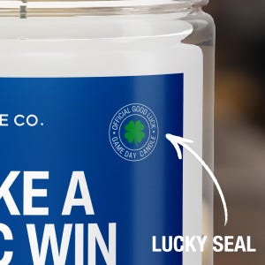 May include: A blue and white candle jar with the text "Take a Win" and a green four-leaf clover with the text "Official Good Luck Game Day Candle".
