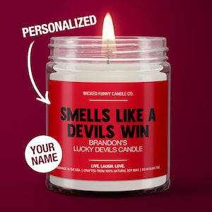 May include: A red and white candle jar with the text "Smells Like A Devils Win" and "Brandon's Lucky Devils Candle". The candle is personalized with the text "Your Name".