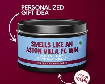 May include: A black and blue candle tin with the text "Smells like an Aston Villa FC win" and "Mark's Lucky Game Day Candle". The text "Winning sure smells good" is also on the tin. The tin is on a maroon background with the text "Personalized Gift Idea" and "Your Name" on either side of the tin.