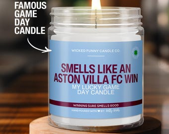 May include: A clear glass candle jar with a white candle inside. The label reads "Smells Like An Aston Villa FC Win My Lucky Game Day Candle" with the company name "Wicked Funny Candle Co." and the text "Winning Sure Smells Good" in a smaller font.