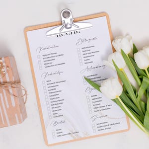 Puede incluir: Una lista de verificaci&oacute;n en un portapapeles con el t&iacute;tulo "Hochzeit" (Boda) en alem&aacute;n. La lista de verificaci&oacute;n incluye categor&iacute;as para "Vorbereitung" (Preparaci&oacute;n), "Kochhilfe" (Ayuda para cocinar), "Getr&auml;nke" (Bebidas), "Essen" (Comida), "Dekoration" (Decoraci&oacute;n), "Sitzordnung" (Organizaci&oacute;n de asientos), "Ankleidung" (Vestimenta), "Anfahrt" (Instrucciones de viaje), "Sonstiges" (Otros). Un ramo de tulipanes blancos se encuentra en la esquina inferior derecha de la imagen.