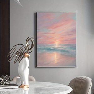 Puede incluir: Una pintura de una puesta de sol rosa y naranja sobre un oc&eacute;ano tranquilo con olas que rompen suavemente en la orilla. El cielo est&aacute; lleno de nubes suaves y esponjosas, y el sol se pone en la distancia, proyectando un c&aacute;lido resplandor sobre la escena.