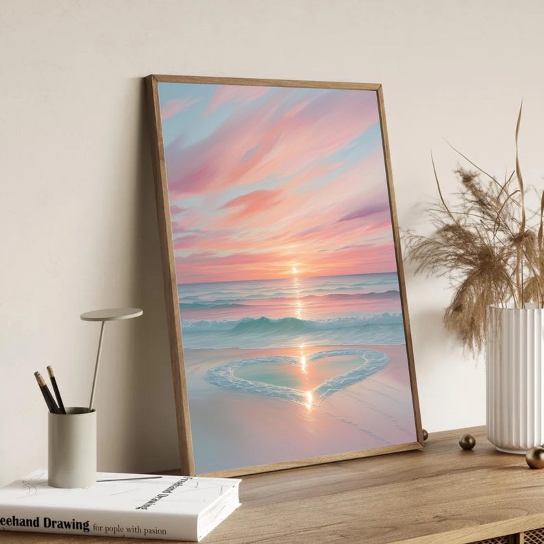 May include: A framed painting of a pink and blue sunset over a beach with a heart shape drawn in the sand.