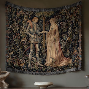 May include: A rectangular woven wall tapestry featuring a dark blue background with a detailed scene of a knight in silver armor and a person in a long cream-colored gown standing together, surrounded by colorful floral and bird motifs.