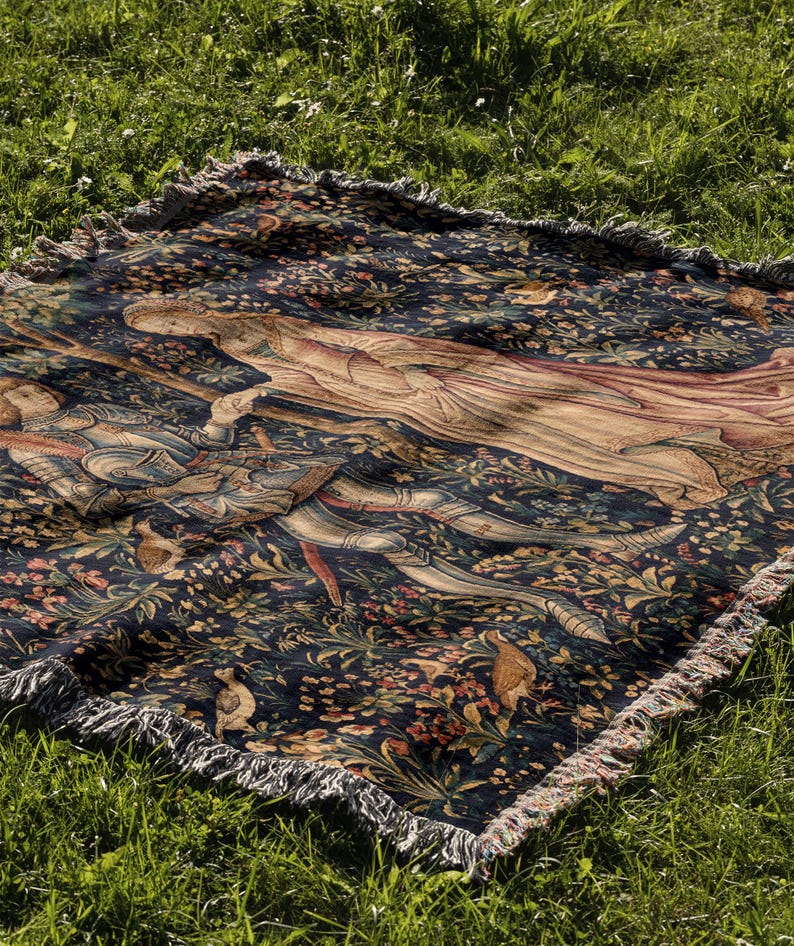 May include: A rectangular woven throw blanket featuring a dark blue background with a detailed scene of a figure in armor and a figure in flowing robes surrounded by colorful floral patterns and small birds, finished with a fringed edge.