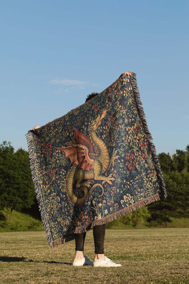 May include: A rectangular woven throw blanket featuring a dark blue background with a detailed illustration of a green dragon breathing fire, surrounded by colorful floral and botanical patterns, finished with a fringed edge on all four sides.