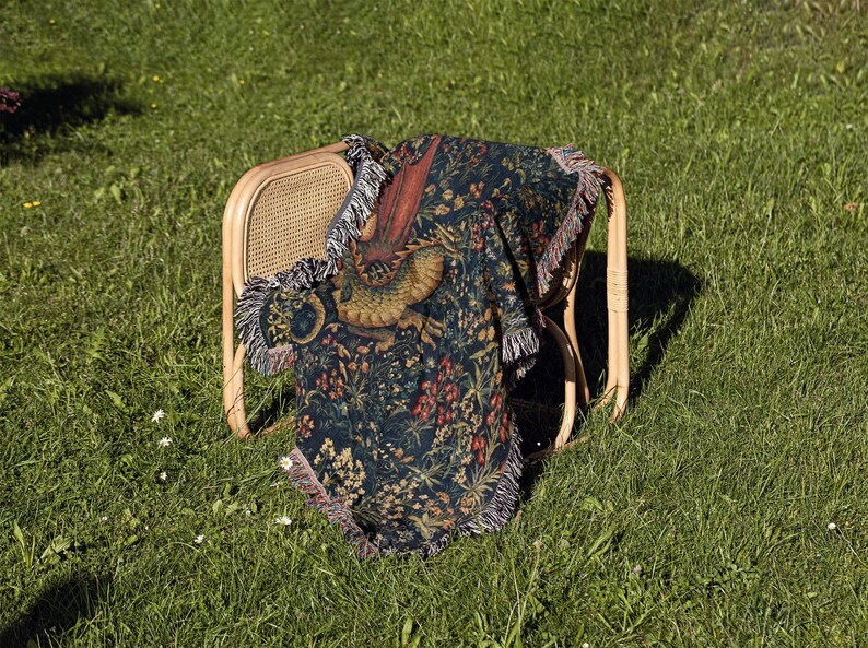 May include: A woven throw blanket featuring a dark blue background with a detailed pattern of a golden dragon, red flowers, and green foliage. The blanket has a fringed edge and is draped over a light-colored wooden chair with a cane back.