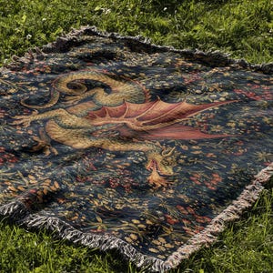 May include: A rectangular woven throw blanket featuring a dark navy blue background with a detailed illustration of a golden dragon with red wings breathing fire, surrounded by a dense pattern of colorful flowers, foliage, and fringed edges.