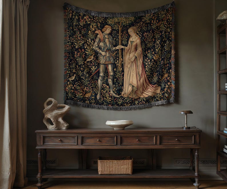 May include: A rectangular woven wall tapestry featuring a dark blue background with a detailed scene of a knight in silver armor and a person in a long cream-colored gown standing together, surrounded by colorful floral and bird motifs.