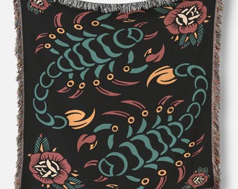 May include: Black throw blanket with a scorpion and rose design. The scorpion is teal, orange, and red. The roses are red, cream, and teal. The blanket has a fringed edge.