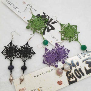 Peut inclure: Trois paires de boucles d'oreilles faites à la main avec des motifs carrés complexes. Les boucles d'oreilles sont faites de fil noir, vert et violet et comportent diverses perles de pierres précieuses.