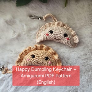 May include: Two crocheted dumpling keychains with smiling faces and pink cheeks. The keychains are beige and tan, with black eyes. The text "Happy Dumpling Keychain - Amigurumi PDF Pattern (English)" is on a red rectangle.
