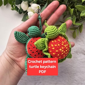 Può includere: Due portachiavi a forma di tartaruga all'uncinetto fatti a mano. Una tartaruga ha un design a forma di anguria con dettagli rossi e neri, l'altra ha un design a forma di fragola con dettagli rossi e gialli. I portachiavi sono verdi e attaccati a un fermaglio argentato. Il testo sull'immagine dice "Crochet pattern turtle keychain PDF".