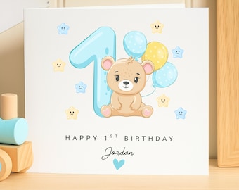 May include: A birthday card with a cartoon bear, balloons, and the number one. The card has the text "Happy 1st Birthday Jordan" with a blue heart. The bear is light brown, and the balloons are blue and yellow.