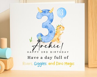 May include: A birthday card featuring a blue number 3, a cartoon dinosaur, and the name "Archie". The card reads "Happy 3rd Birthday" and "Have a day full of Roars, Giggles, and Dino Magic."